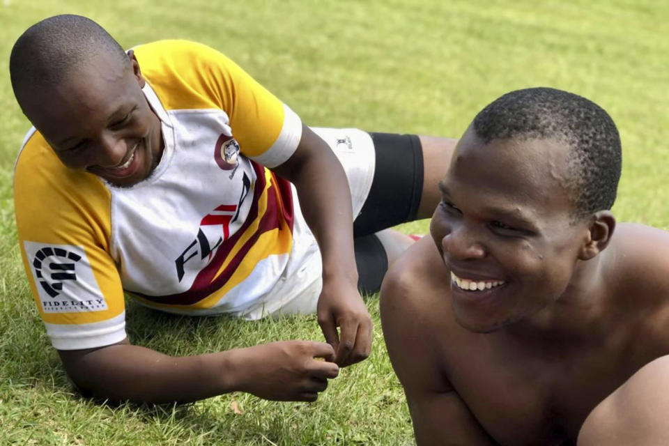 In this undated photo provided by Lindsay Myeni, is Lindani Myeni, foreground with no shirt on, resting on the grass after a rugby match in Eshowe, South Africa. Myeni was fatally shot by Honolulu police in 2021 after he physically attacked officers, who responded when an upset occupant of a home complained a stranger had entered uninvited wearing a feathered headband and made bizarre comments. Results of studies of Myeni's brain tissue, obtained by The Associated Press, show the 29-year-old South African rugby player had Stage 3 CTE, or brain trauma caused by repeated concussions. (Lindsay Myeni via AP)
