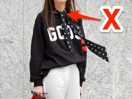 red x and arrow pointing at person standing next to a building wearing a skinny polka dot scarf with a sweatshirt and white wideleg pants