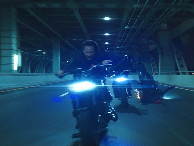 Keanu Reeves as John Wick on a motorbike.