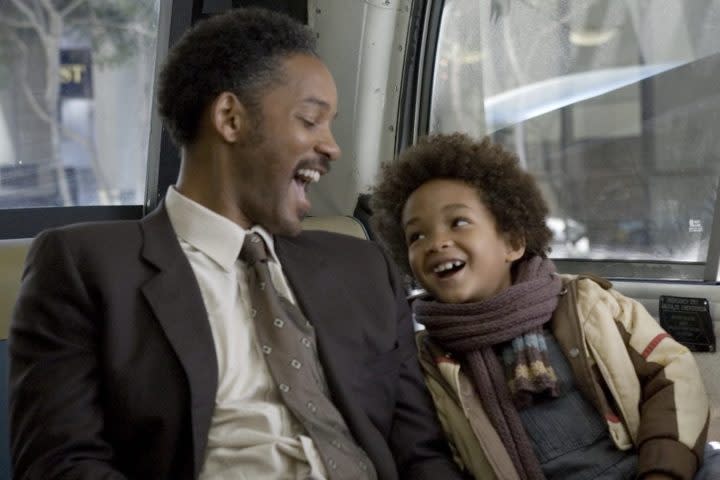 A man on a bus seat laughs with his son sitting next to him.