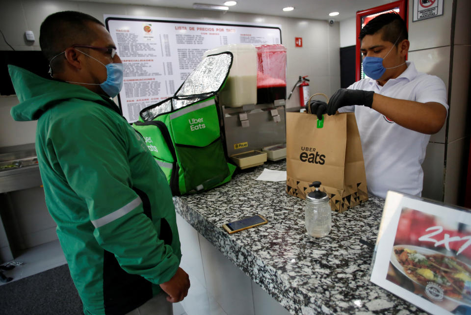 Un vendedor, con una máscara protectora, entrega alimentos al trabajador de Uber Eats, mientras continúa el brote de la enfermedad por coronavirus (COVID-19). REUTERS / Gustavo Graf