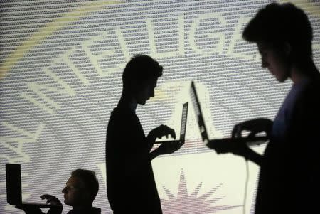 People are silhouetted as they pose with laptops in front of a screen projected with binary code and a Central Inteligence Agency (CIA) emblem, in this picture illustration taken in Zenica October 29, 2014. REUTERS/Dado Ruvic