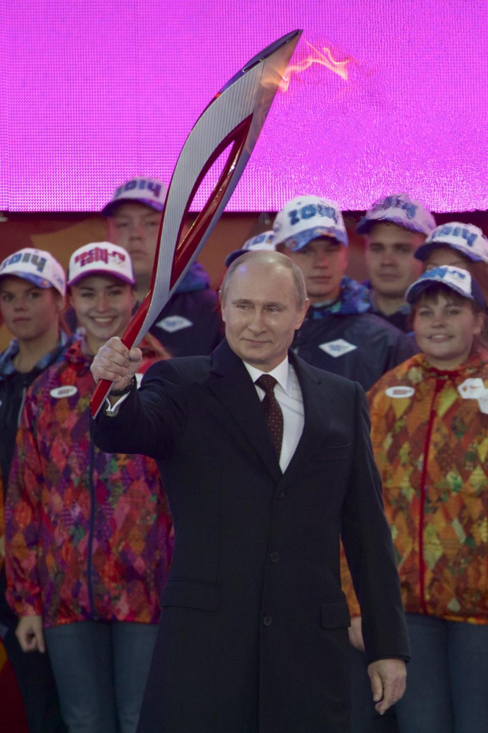 FILE - In this Sunday, Oct. 6, 2013 file photo Russian President Vladimir Putin smiles while ceremonially lighting the Olympic flame with a torch at Moscow's Red Square prior to the 123-day torch relay to Sochi for the 2014 Winter Olympic Games. For President Vladimir Putin, the Winter Olympics he brought to Sochi have always been about far more than sports. The benefits he sees from holding the games range from improving Russia’s international standing and instilling a sense of national pride to turning around the country’s demographic decline. And of course Putin wants to be seen, at home and abroad, as the man who made this all possible. (AP Photo/Ivan Sekretarev, File)