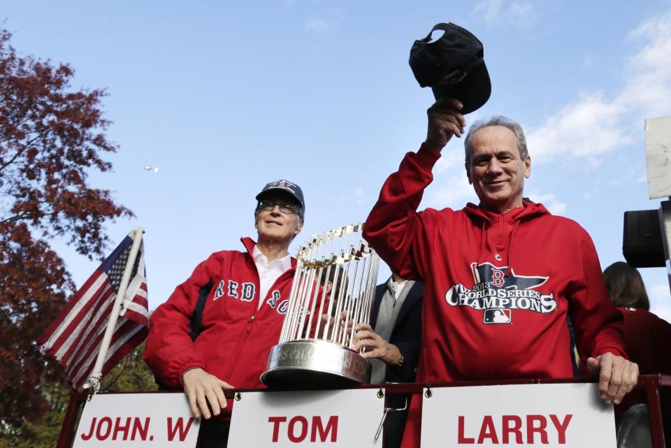 FILE - Boston Red Sox president Larry Lucchino, right, tips his cap to fans as majority owner John Henry holds the 2013 World Series championship trophy during a parade in celebration of the baseball team's win, Saturday, Nov. 2, 2013, in Boston. Larry Lucchino, the force behind baseball’s retro ballpark revolution and the transformation of the Boston Red Sox from cursed losers to World Series champions, has died. He was 78. Lucchino had suffered from cancer. The Triple-A Worcester Red Sox, his last project in a career that also included three major league baseball franchises and one in the NFL, confirmed his death on Tuesday, April 2, 2024. (AP Photo/Charles Krupa, File)