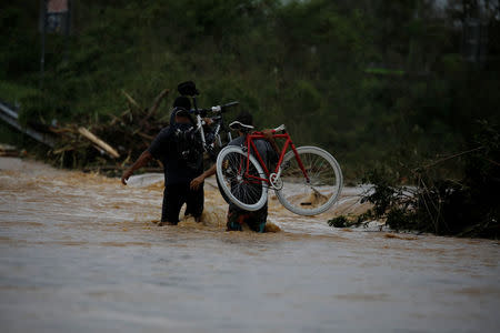 Men carrying bicycles wade through a flooded road after the area was hit by Hurricane Maria in Yauco, Puerto Rico September 21, 2017. REUTERS/Carlos Garcia Rawlins