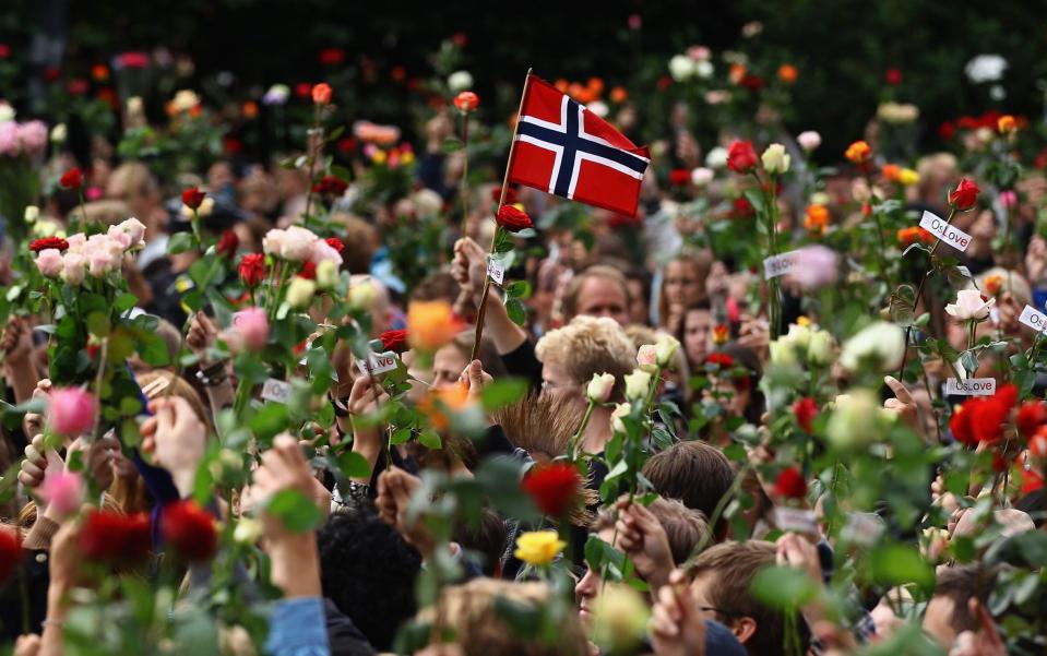 A Norwegian flag is held up amidst flowers as an estimated 100,000 people gather in Oslo town centre for a vigil following Friday's twin extremist attacks on July 25, 2011 in Oslo, Norway - Jeff J Mitchell/Getty Images