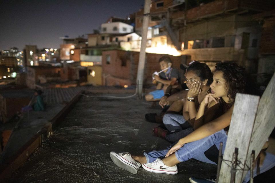 Residents sit on their roof to watch the film Aladdin projected on a screen set up on the roof of a neighbor's home in the Petare neighborhood of Caracas, Venezuela, late Monday, June 1, 2020. A neighborhood group called The Download Zone set up the movie as a free entertainment option for families cooped up since mid-March under the COVID-19 quarantine. (AP Photo/Ariana Cubillos)