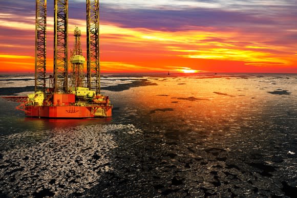 An offshore drilling rig at sunrise over a frozen sea.