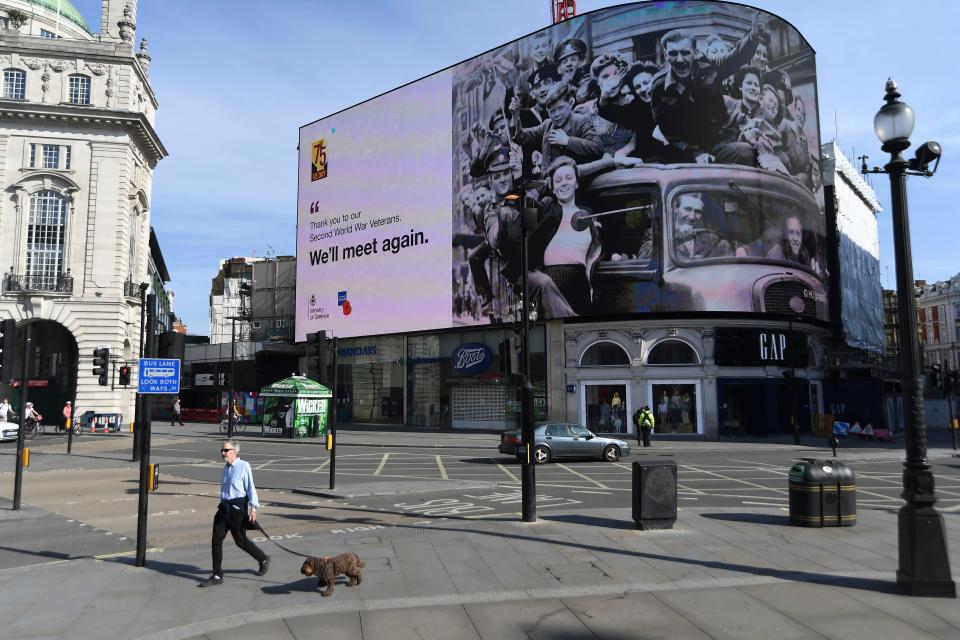 A man walks a dog near a Victory in Europe Day tribute displayed on one of the screens in London's Piccadilly Circus on May 8, 2020 on the 75th anniversary of the end of World War II in Europe.