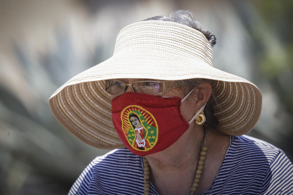 A woman wears a mask with a religious figure as she prays the rosary in the aftermath of a morning fire at the San Gabriel Mission, Saturday, July 11, 2020, in San Gabriel, Calif. The fire destroyed the rooftop and most of the interior of the nearly 250-year-old California church that was undergoing renovation. (AP Photo/Marcio Jose Sanchez)