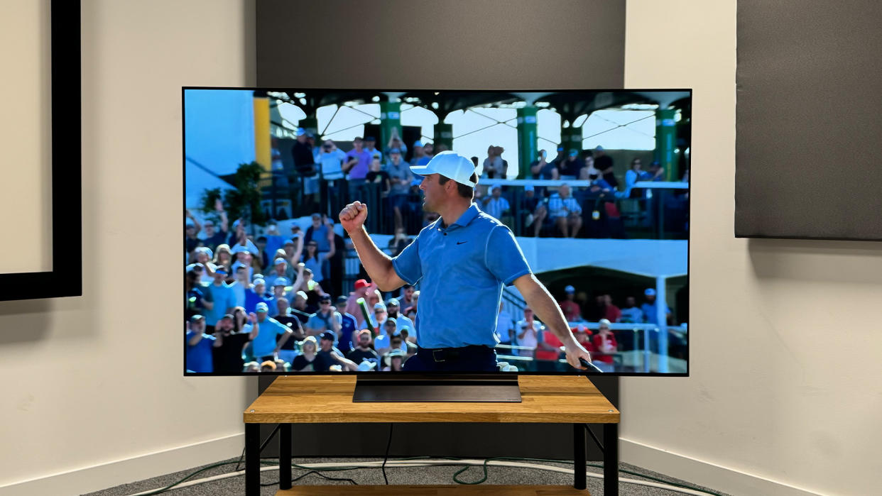  65-inch LG C4 TV photographed straight-on on a wooden stand. On the screen is an image of a golfer celebrating. 