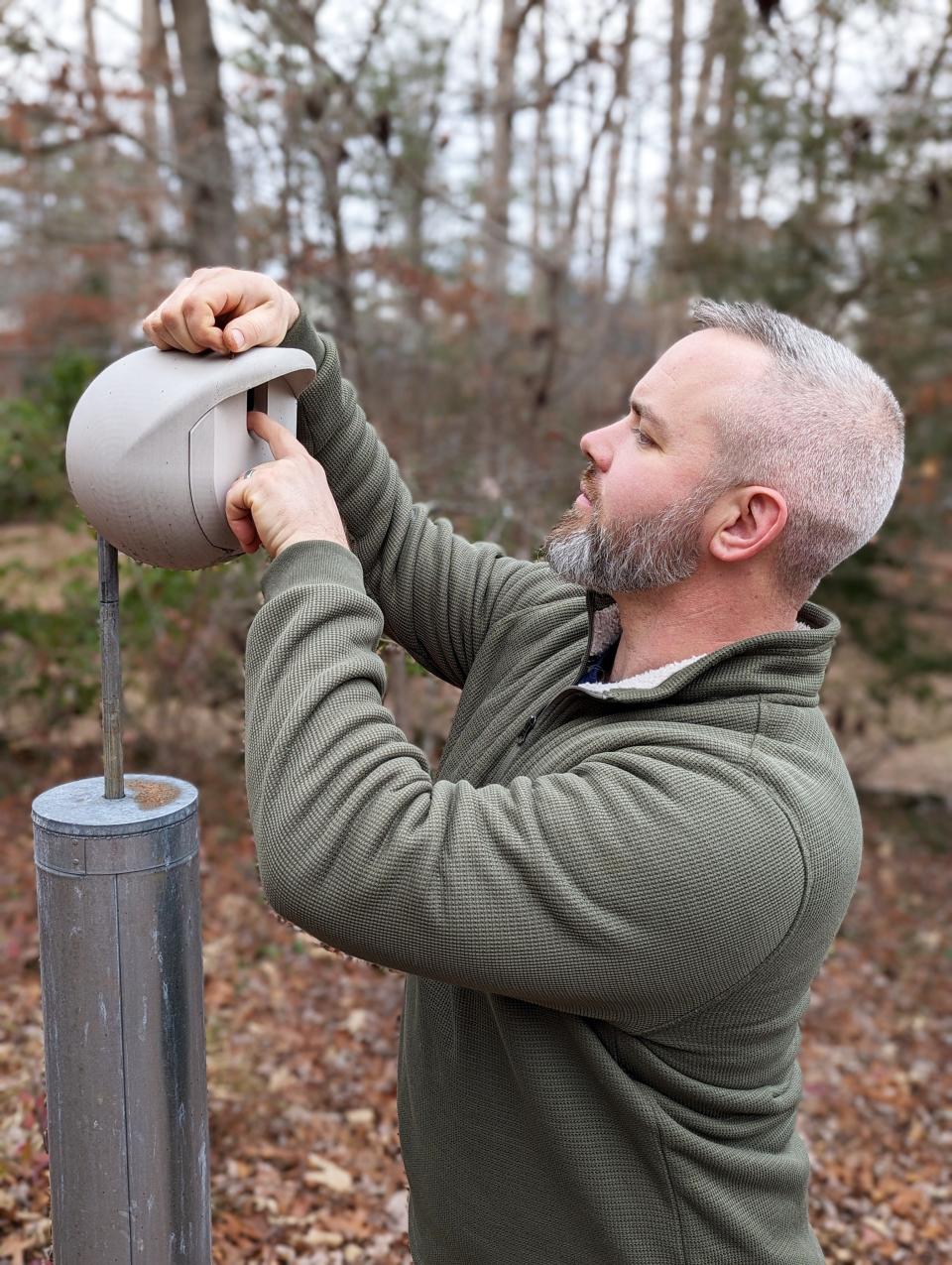 The Oak Ridge Bird Man Luke Coe-Starr inspects the Borbhouse, a bird nest box he designed and 3D-printed. In the background are crows in the woods.