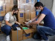 Volunteers wearing protective masks and gloves fill boxes with food for distribution to people in need, in Beirut