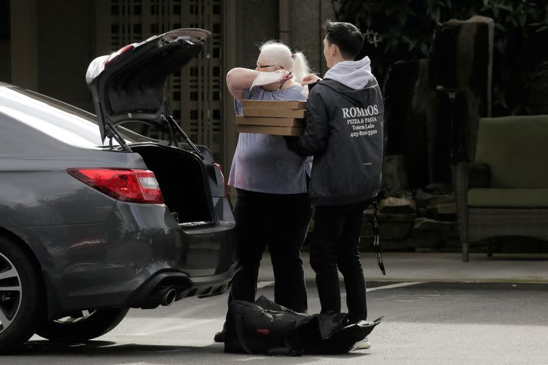 FILE PHOTO: A worker coughs into her arm as she accepts pizza from a delivery driver at the Life Care Center of Kirkland, where two of three confirmed coronavirus cases in the state had links to the long-term care facility in Kirkland