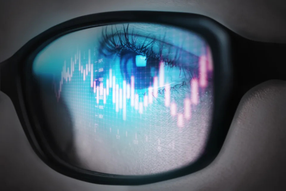 The reflection of the stock graph on a young adult women&#39;s glasses.