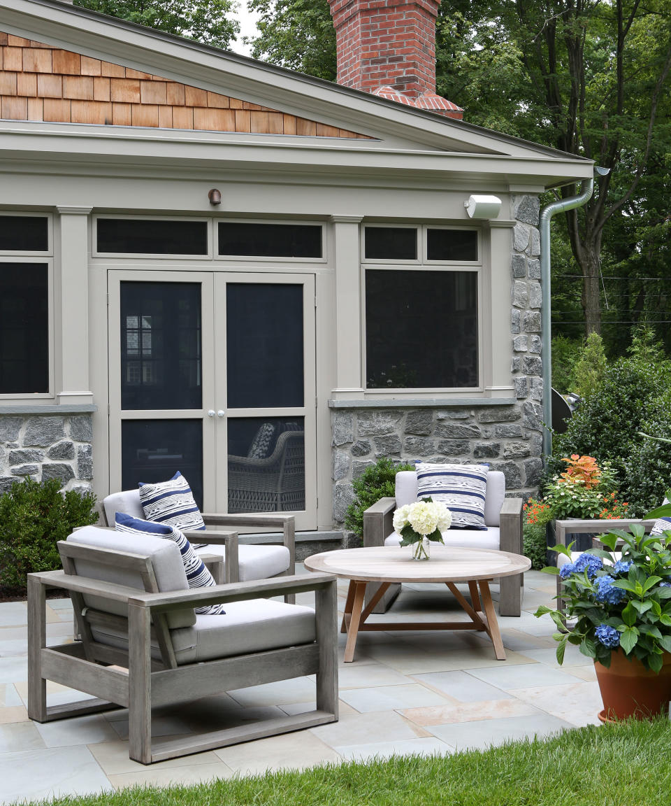 Small back yard landscaping ideas featuring a pale gray patio with gray wooden chairs around a circular coffee table, with potted hydrangeas.