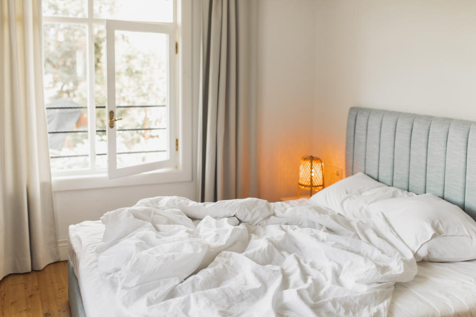 Unmade bed in a cozy bedroom with sunlight streaming through a window, creating a warm and intimate atmosphere