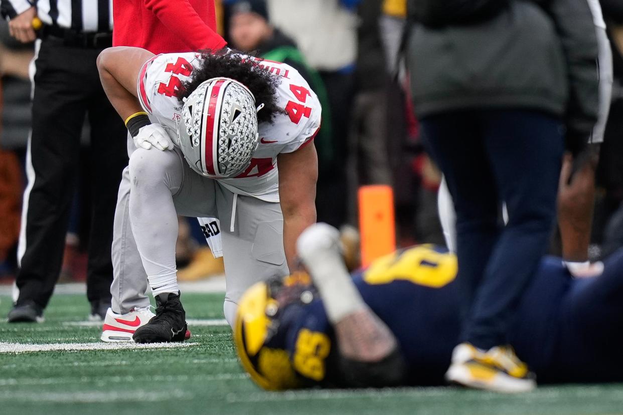 Nov 25, 2023; Ann Arbor, Michigan, USA; Ohio State Buckeyes defensive end JT Tuimoloau (44) kneels as Michigan Wolverines offensive lineman Zak Zinter (65) is tended to by medics after an injury during the second half of the NCAA football game at Michigan Stadium. Ohio State lost 30-24.
