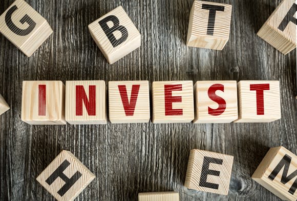 The word "invest" spelled out in red on wood blocks.