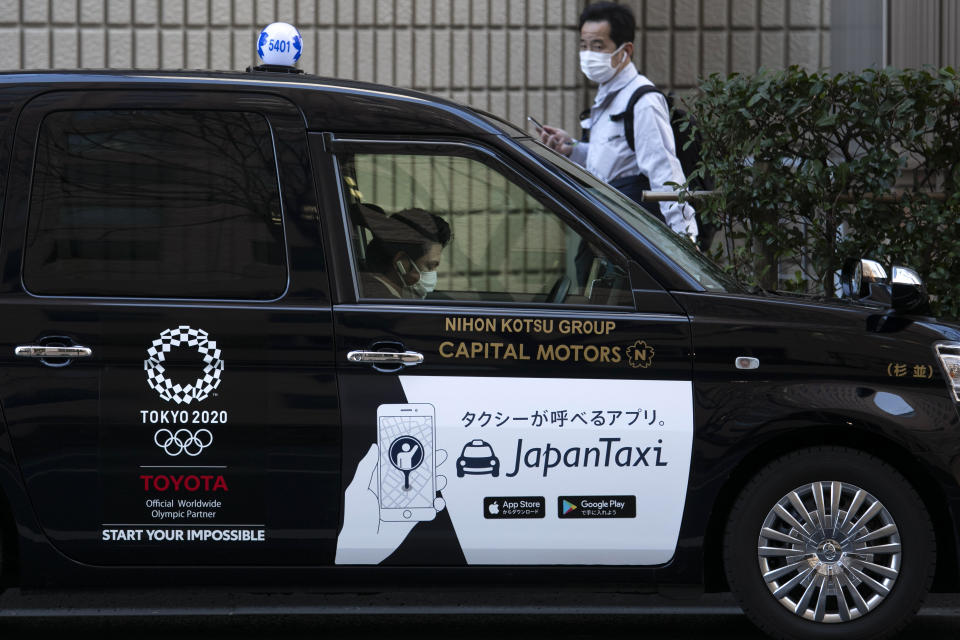 FILE - In this Tuesday, Feb. 18, 2020, file photo, a taxi driver wearing a mask waits for a fare with a Tokyo 2020 logo on the door of his car in Tokyo. The Tokyo Olympics open in exactly five months on July 24. But the fast-spreading coronavirus from China is making Tokyo organizers very anxious. Three deaths have been reported in Japan with more than 700 cases, more than 600 from a cruise ship that docked in Japan. (AP Photo/Jae C. Hong, File)