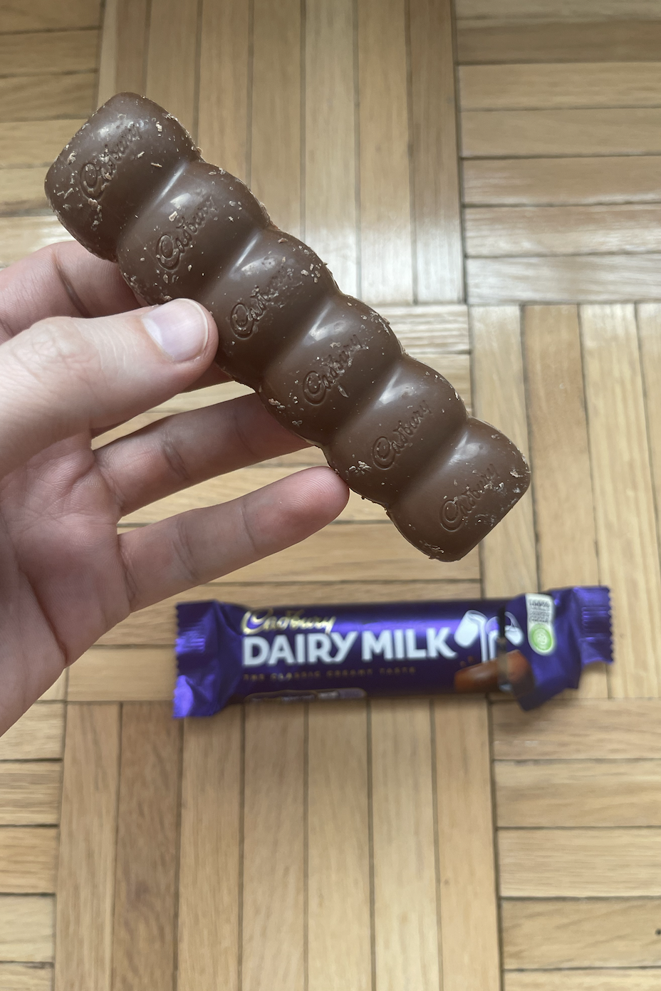 Hand holding a Cadbury Dairy Milk chocolate bar with its wrapper partially visible