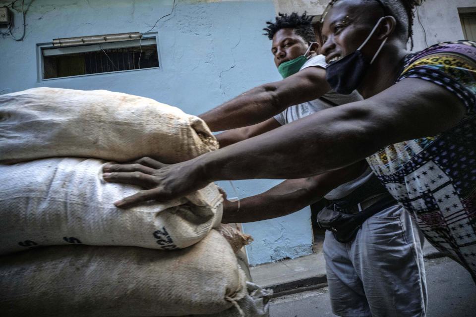 FILE - In this Dec. 23, 2020 file photo, workers wearing ill-fitting masks used to curb the spread of the new coronavirus push a cart loaded with sacks in Havana, Cuba. In 2021, the government is implementing a deep financial reform that reduces subsidies, eliminates a dual currency that was key to the old system, and raises salaries, in hopes of boosting productivity to help alleviate an economic crisis and reconfigure a socialist system that will still grant universal benefits such as free health care and education. (AP Photo/Ramon Espinosa, File)