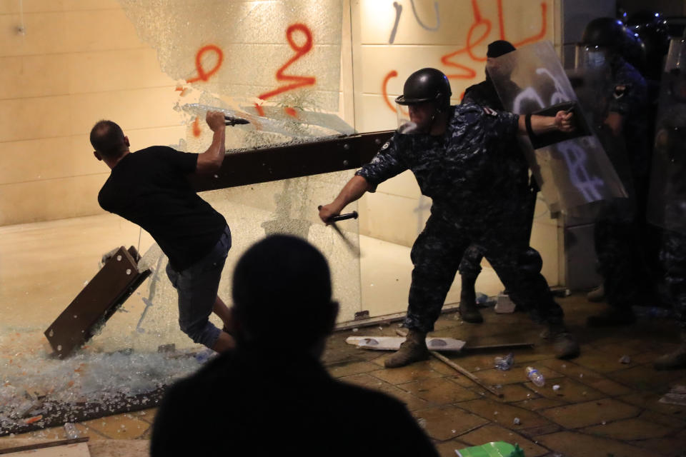 A riot policeman, right, beats a supporter of relatives of people who were killed in last year's massive blast at Beirut's seaport, who is destroying the glass door of an apartment building entrance where caretaker Interior Minister Mohamed Fehmi lives during a protest demanding an end to what they call the obstruction of an investigation into one of the largest non-nuclear explosions in history, in Beirut, Lebanon, Tuesday, July 13, 2021. Riot police fired tear gas and scuffled with protesters mostly family members of victims of the Beirut Port blast outside the home of Lebanon's caretaker interior minister Tuesday. (AP Photo/Hussein Malla)