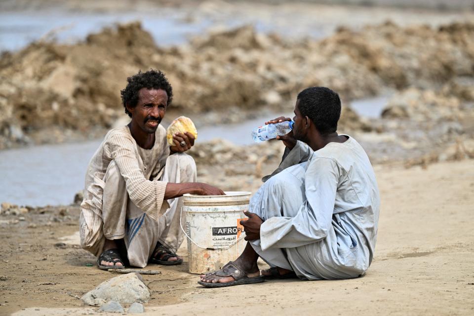 A man drinks water while another holds a loaf of bread, following devastating floods, in Arbaat, Sudan near Port Sudan (REUTERS)