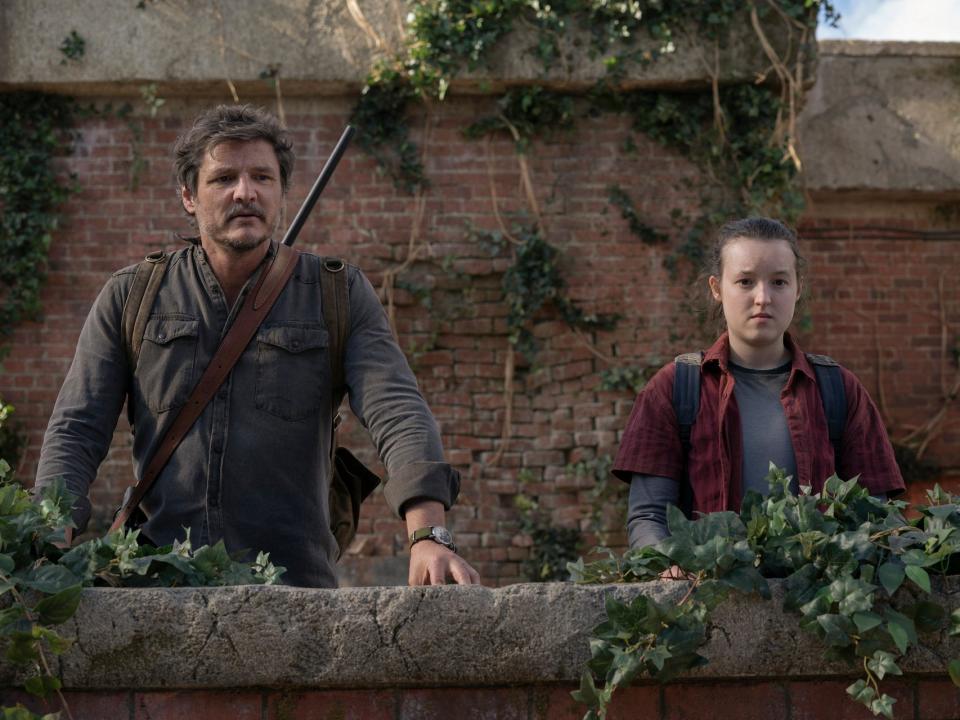 TLOU 109, The Last of Us season one, episode nine. joel and ellie in the last of us finale. they're standing at a ledge on what seems to be a building roof, looking out over the greenery that's grown there in humanity's absence. joel has a rifle strapped to his back, while ellie looks solemn