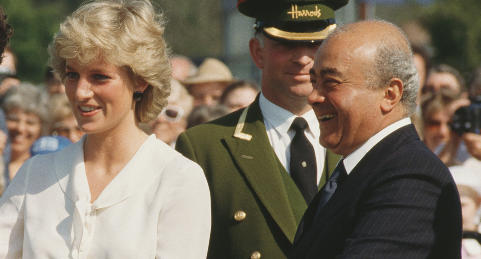 Princess Diana (left) and Mohamed Al-Fayed (right) smile as a man in a Harrods uniform stands behind them.