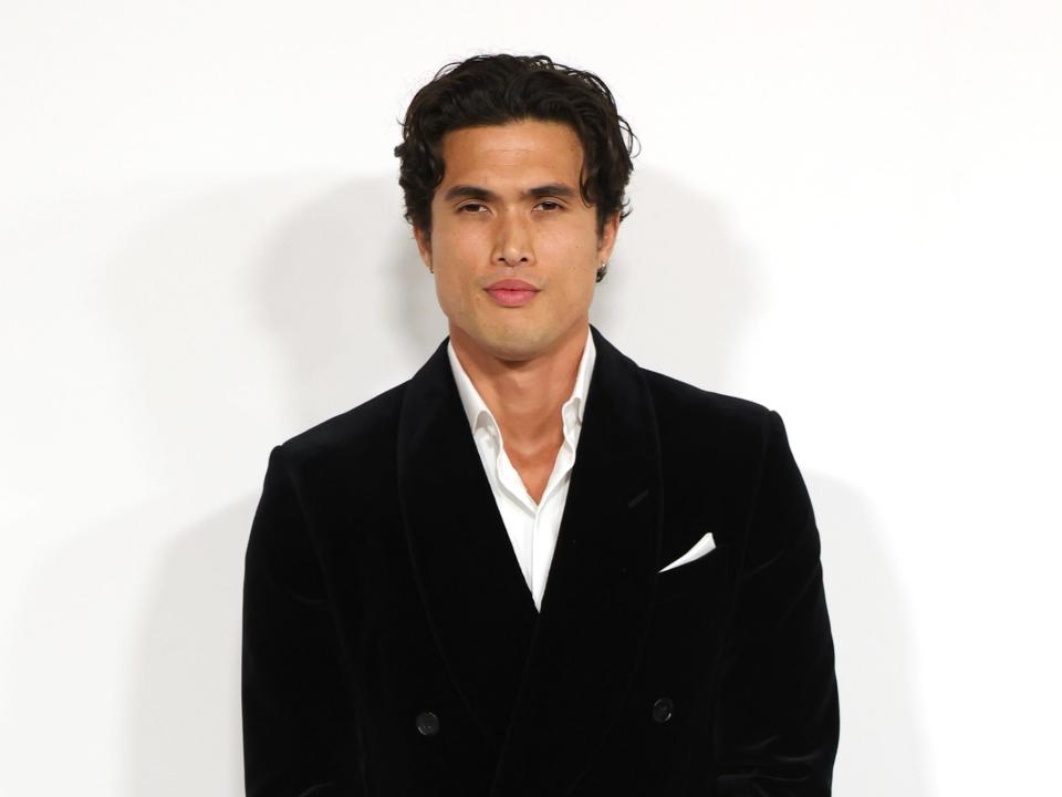 charles melton in a black suit and white shirt, holding his hands together