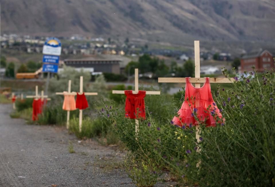 Children's red dresses are staked along a highway near the former Kamloops Indian Residential School.