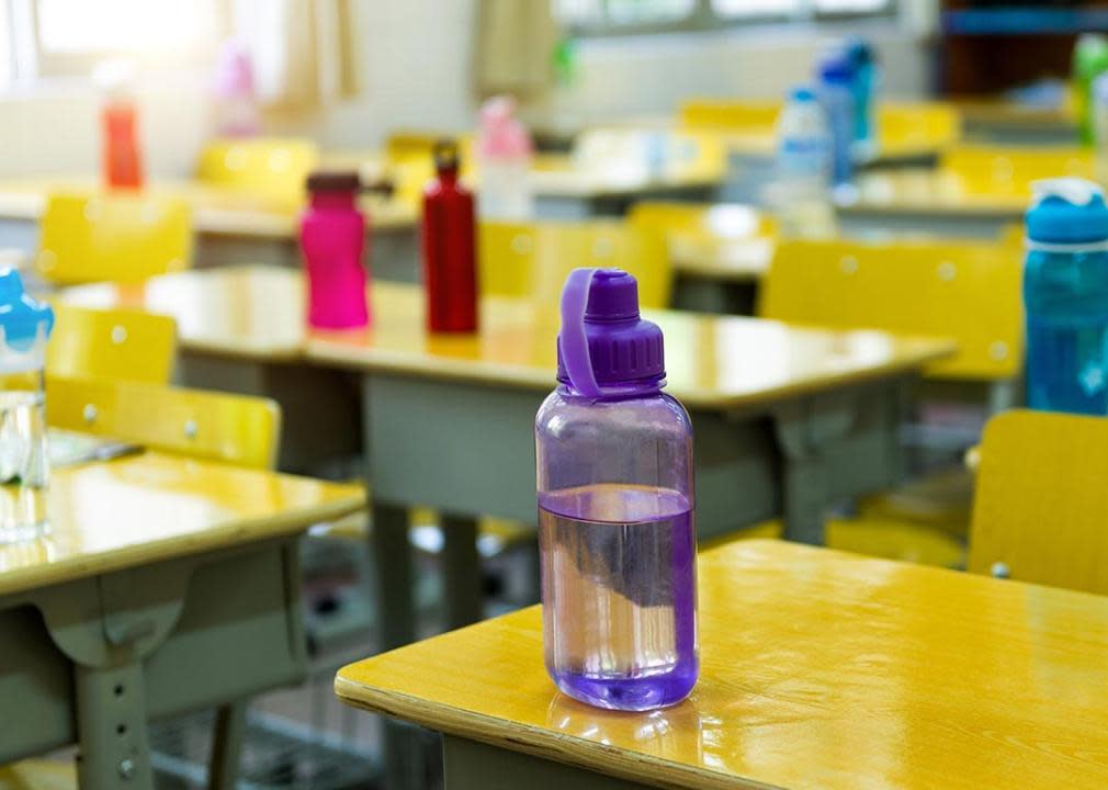 Different colored water bottles sit on yellow desks in a classroom.