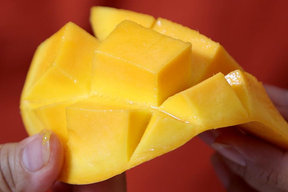 Helen Castillo holds a side of a mango after cutting it into cubes. Thursday, July 21, 2022