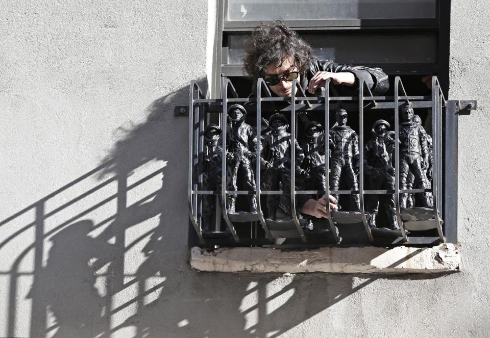 This Oct. 24, 2013 photo shows The Strokes' drummer Fabrizio Moretti arranging cast-in-plastic astronauts on the fire escape of an second story apartment above his public art installation outside the SoHo Rag & Bone store in New York. The installation is part of the clothing brand's ongoing urban art project, in which artists revamp the store's façade. But for Moretti, it's a chance to revisit his long latent background. (AP Photo/Kathy Willens)