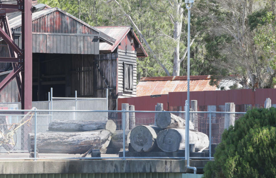 Old wooden shack with a corrugated metal roof, surrounded by a wire fence and logs piled nearby