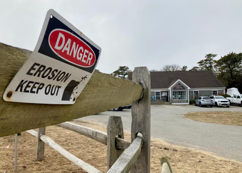 An erosion warning sign at the Monomoy National Wildlife Sanctuary in Chatham with the soon-to-be demolished visitor center in the background.