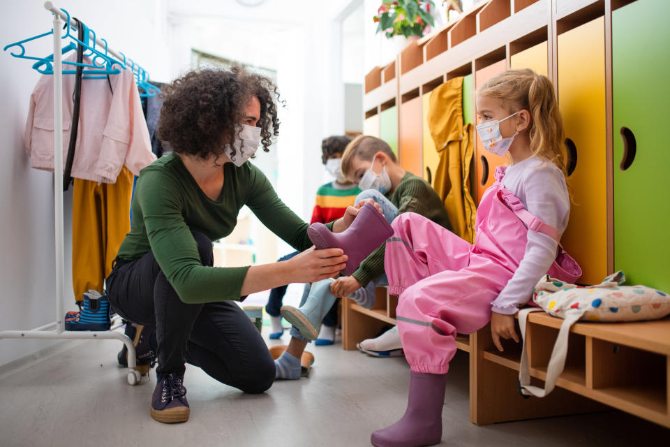 Photo of a teacher helping a small child put on a rainboot