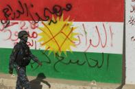 A member of the Iraqi forces walks past a defaced Kurdish flag on the outskirts of Kirkuk on October 16, 2017