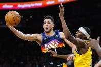 Phoenix Suns guard Devin Booker (1) passes the ball to a teammate as Indiana Pacers forward Justin Holiday, right, defends during the second half of an NBA basketball game Saturday, Jan. 22, 2022, in Phoenix. (AP Photo/Ross D. Franklin)