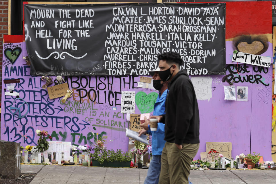 Two people walk past a memorial Sunday, June 28, 2020, in Seattle, for people of color believed to have died in police custody, where several streets are blocked off in what has been named the Capitol Hill Occupied Protest zone. Seattle Mayor Jenny Durkan met with demonstrators Friday after some lay in the street or sat on barricades to thwart the city's effort to dismantle the protest zone that has drawn scorn from President Donald Trump and a lawsuit from nearby businesses. (AP Photo/Elaine Thompson)