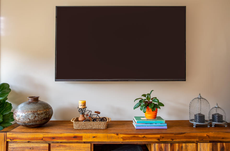 Television on a wall above a wooden console with decorative items and plants