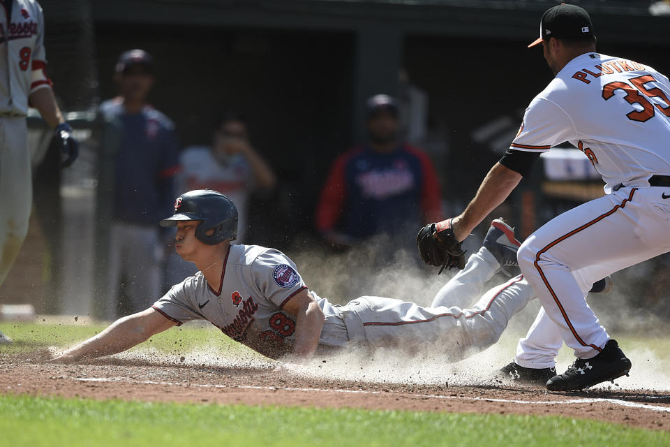 Minnesota Twins' Rob Refsnyder, left, slides across the plate as Baltimore Orioles pitcher Adam Plutko covers in the 10th inning of a baseball game Monday, May 31, 2021, in Baltimore. Refsnyder was safe, scoring the go-ahead run on a wild pitch. (AP Photo/Gail Burton)