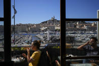 People enjoy a coffee on a balcony in the Old Port of Marseille in southern France, Tuesday, May 7, 2024. The Olympic torch will finally enter France when it reaches the southern seaport of Marseille on Wednesday. (AP Photo/Daniel Cole)