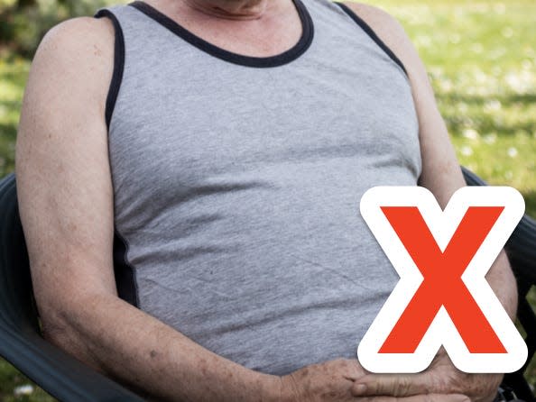 red x over older man's gray undershirt as he poses for a photo outside in a backyard