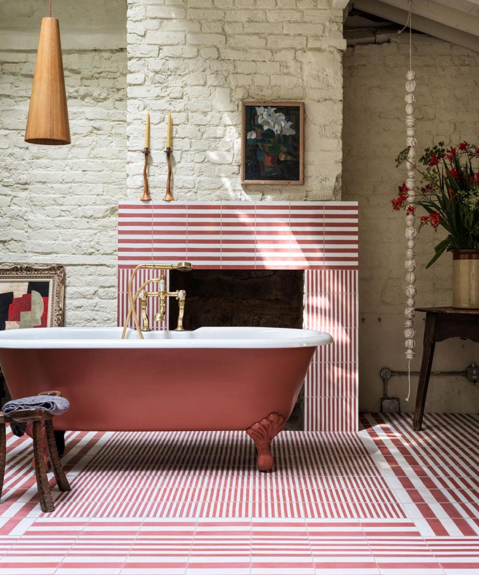 red and white bathroom with striped tiles and a red freestanding rolltop in the middle