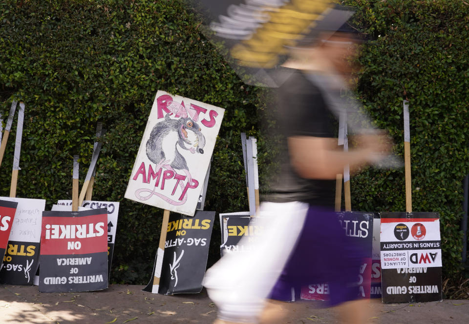 A picketer blurs past protest signs outside Walt Disney Studios, Wednesday, Sept. 6, 2023, in Burbank, Calif. The film and television industries remain paralyzed by Hollywood's dual actors and screenwriters strikes. (AP Photo/Chris Pizzello)