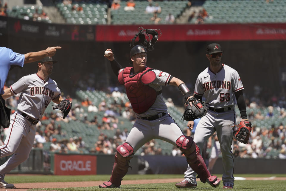 Arizona Diamondbacks catcher Carson Kelly, center, throws out San Francisco Giants' Kevin Gausman (not shown) at first base after a sacrifice bunt in the fourth inning of a baseball game Thursday, June 17, 2021, in San Francisco. Diamondbacks relief pitcher Riley Smith, left, and first baseman Christian Walker, right, look on. (AP Photo/Eric Risberg)