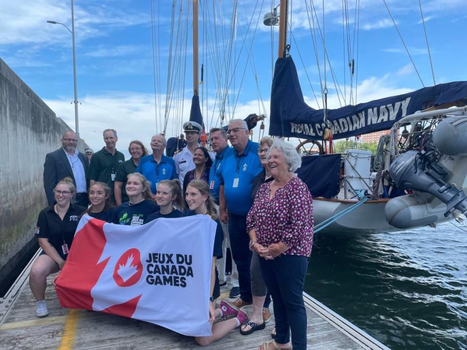 Canada Games organizers, volunteers and athletes show off the Canada Games flag in front of HMCS Oriole on Wednesday.  (Sheehan Desjardins/CBC - image credit)