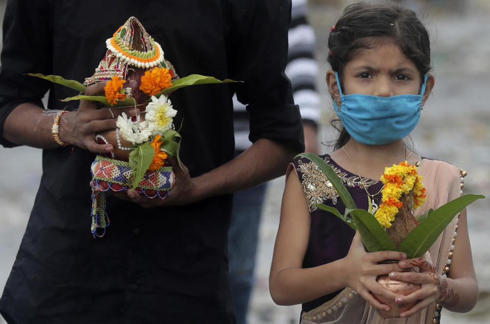A girl wears a mask as members of the fishing community offer prayers during Narali Purnima festival on the Arabian Sea coast in Mumbai, India, Monday, Aug. 3, 2020. Narali Purnima also known as Coconut Day, is celebrated majorly by the fishing community in the western coastal regions of India. (AP Photo/Rafiq Maqbool)